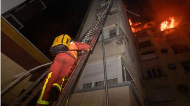 This handout picture taken and released by the Paris firefighters brigade in the night of February 5, 2019 shows a fireman climbing up a ladder as a fire burns in a building in Erlanger street in the 16th arrondissement in Paris