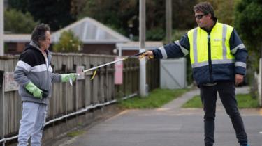 A man is given an appointment slip by a security guard using a stick outside a COVID-19 coronavirus clinic