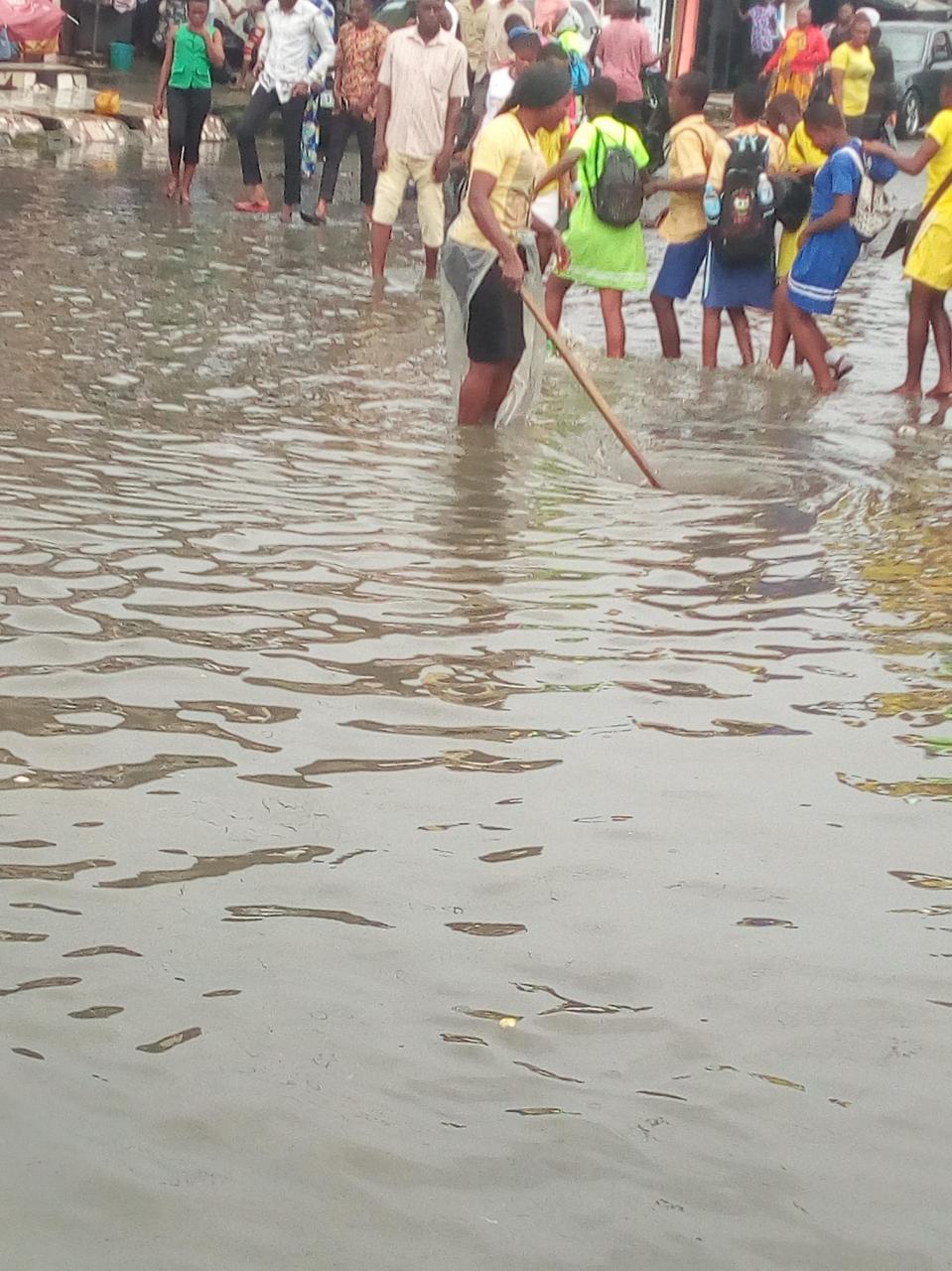 Lady spotted under the rain helping school children cross flooded market in Port Harcourt