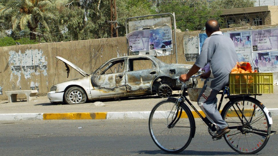 An Iraqi man rides a bicycle passing by a remains of a car burnt during a deadly incident involving Blackwater guards in Baghdad in September 2007