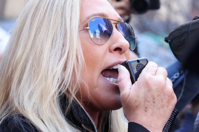 Marjorie Taylor Greene in aviator sunglasses, speaking into the mouthpiece of a bullhorn