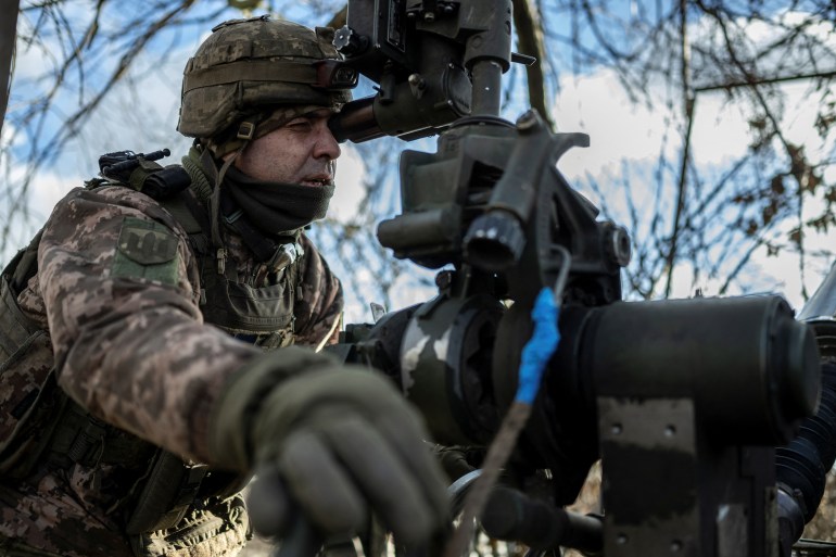 A Ukrainian soldier preparing to fire an M777 howitzer towards Russian troops on the front line. He is looking into the sight and moving the weapon with his right hand
